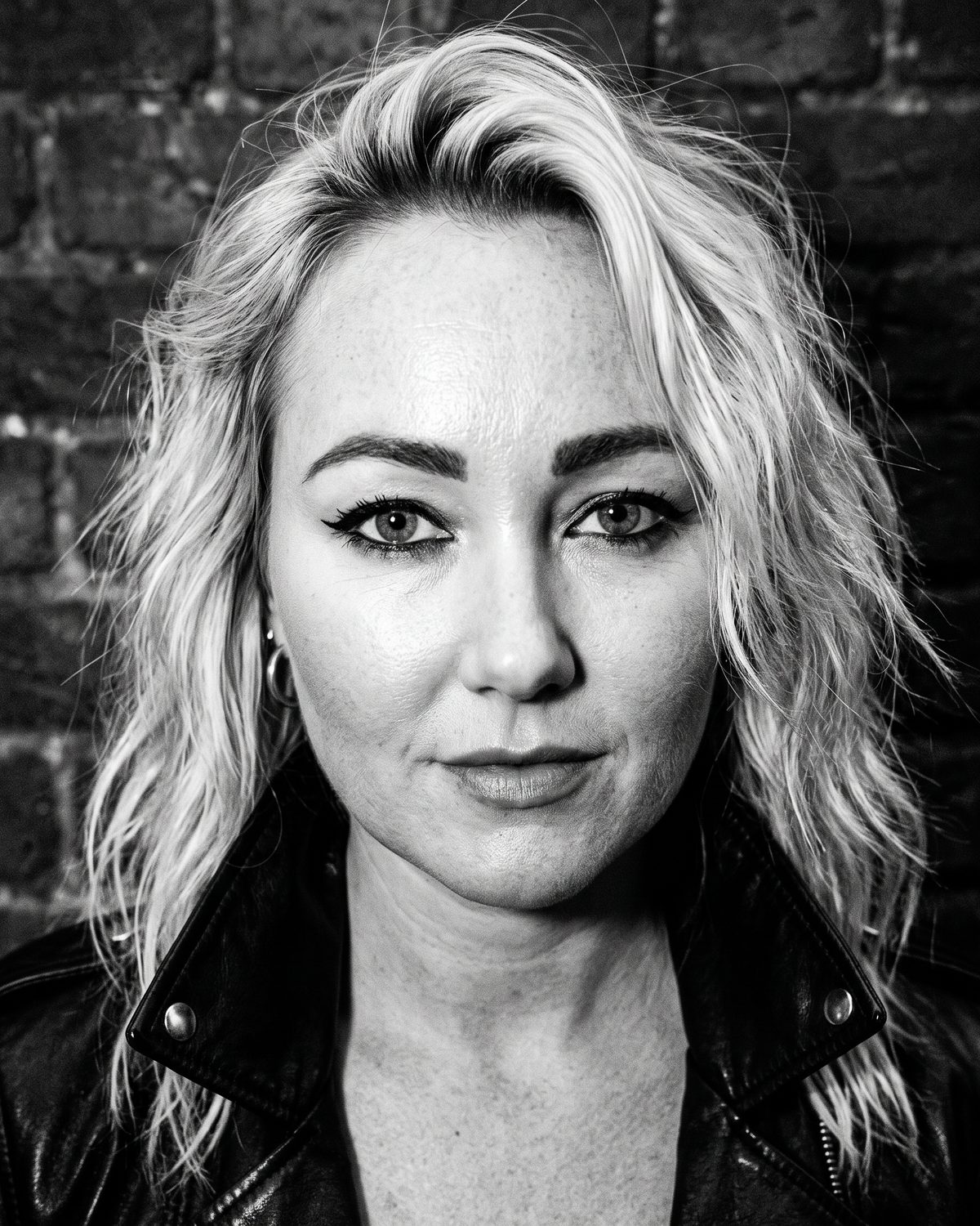 Black-and-white close-up of Jessie Riot with messy blonde hair and dark eyeliner, looking into the camera.